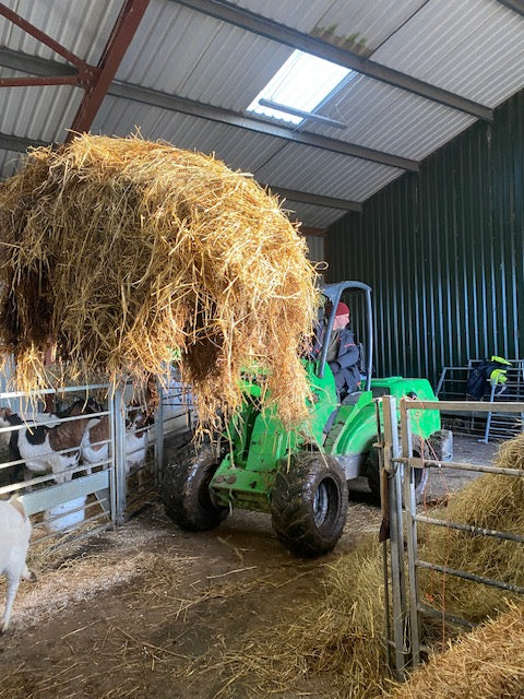 Green Avant Loader carrying hay in the barn.